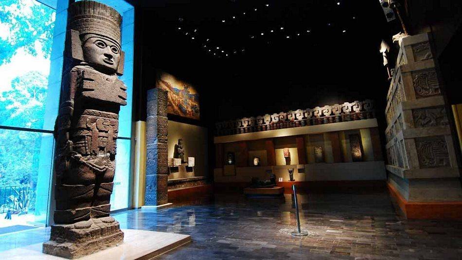 Escultura de piedra del Atlante de Tula en la Sala Tolteca del Museo Nacional de Antropología junto a un gran ventanal
