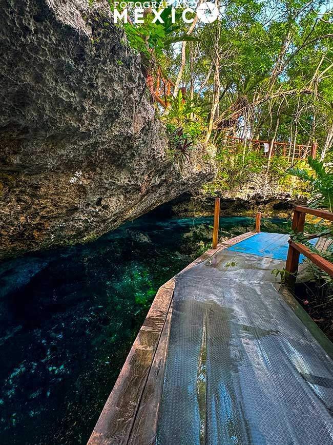 Plataforma de madera con suelo antideslizante junto al agua azul transparente bajo una gran pared de roca.