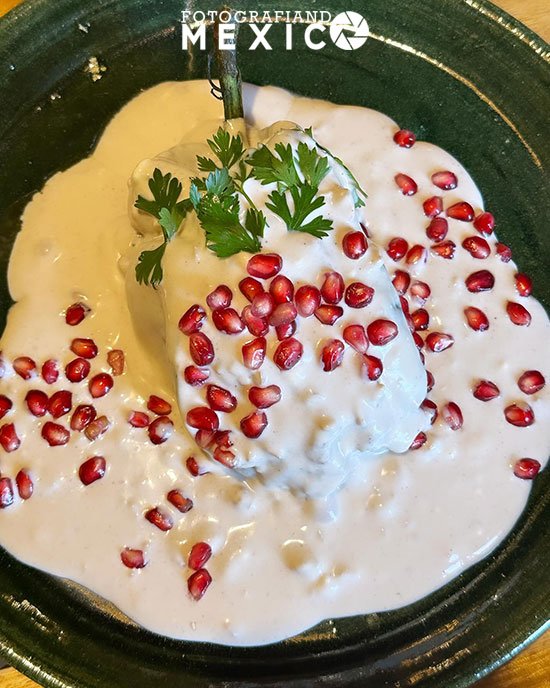 Plato de chiles en nogada cubiertos con salsa de nuez, granada y perejil