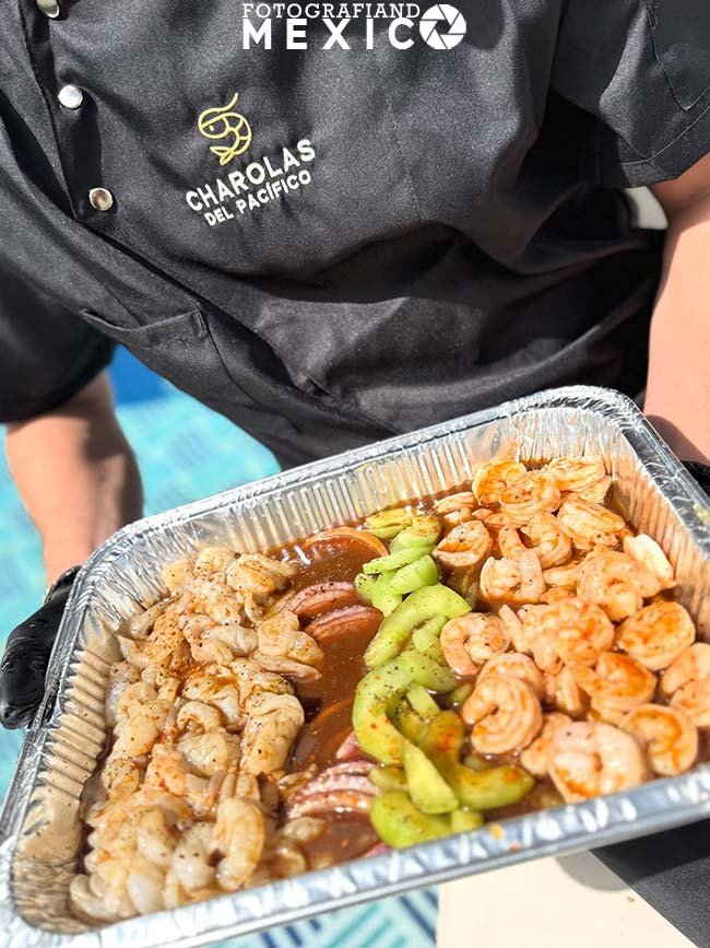 Bandeja con camarones frescos curtidos acompañados de rebanadas de pepino y cebolla morada en salsa oscura de mariscos.